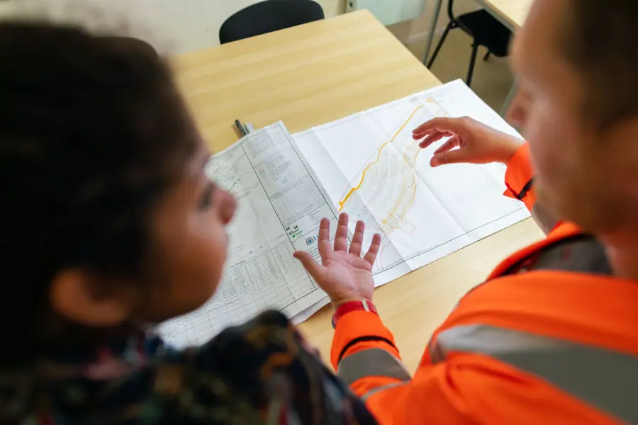 Engineer in hi-vis going through solar layout drawings with a client at a desk before consents are applied for