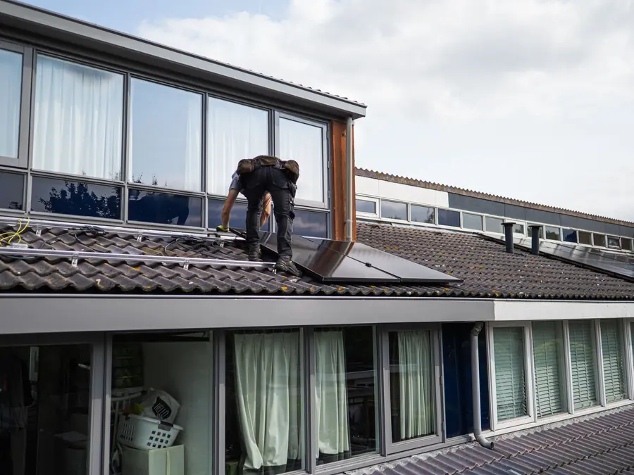 Installer kneeling on a pitched commercial roof fitting solar panels within permitted development height limits