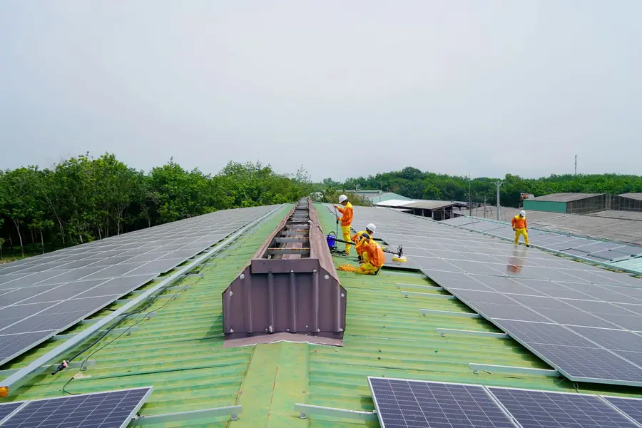 Team of installers in hi-vis fitting rows of solar panels across a large industrial roof under a grey sky