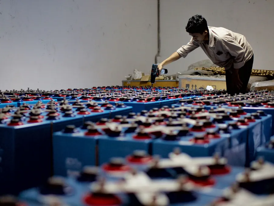 Technician checking racks of lithium battery modules in a plant room during a commercial battery storage installation