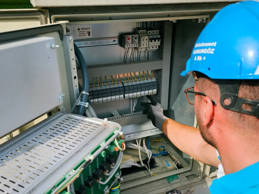 Electrician in a hard hat testing connections inside an electrical cabinet during a maintenance visit