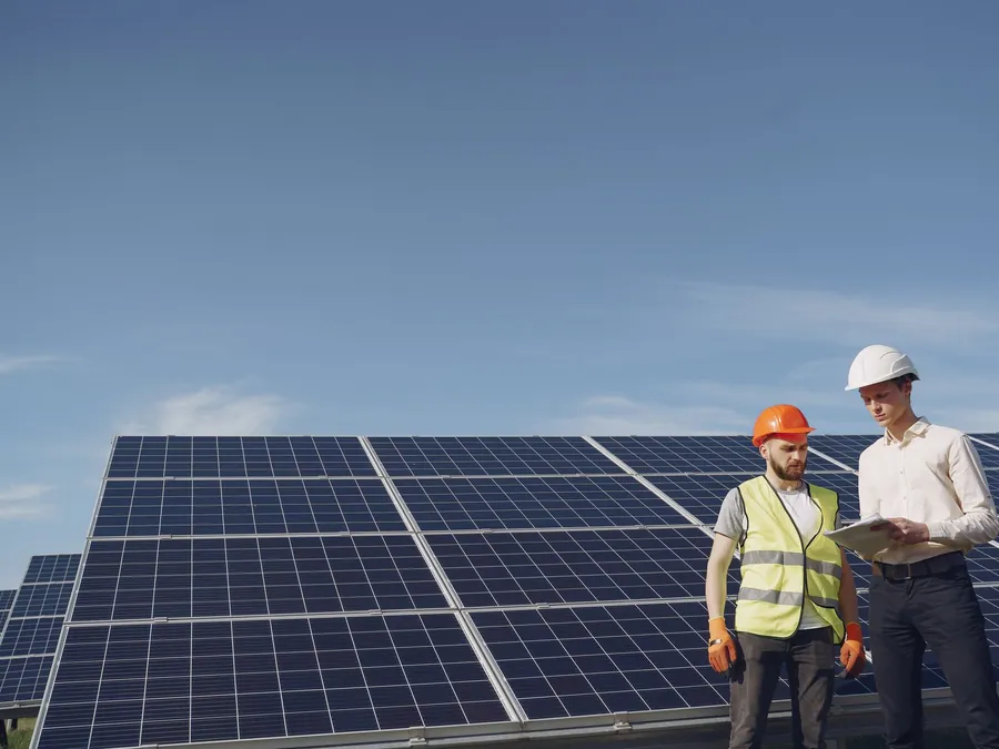 Two engineers in hi-vis and hard hats going through paperwork beside a ground-mounted solar array