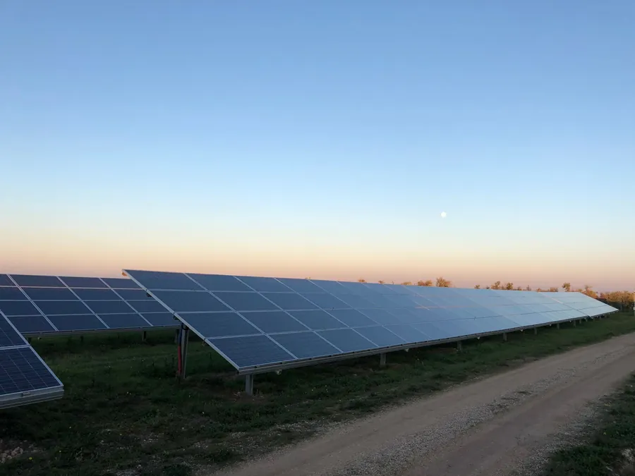 Rows of ground-mounted solar panels beside a gravel track at dusk