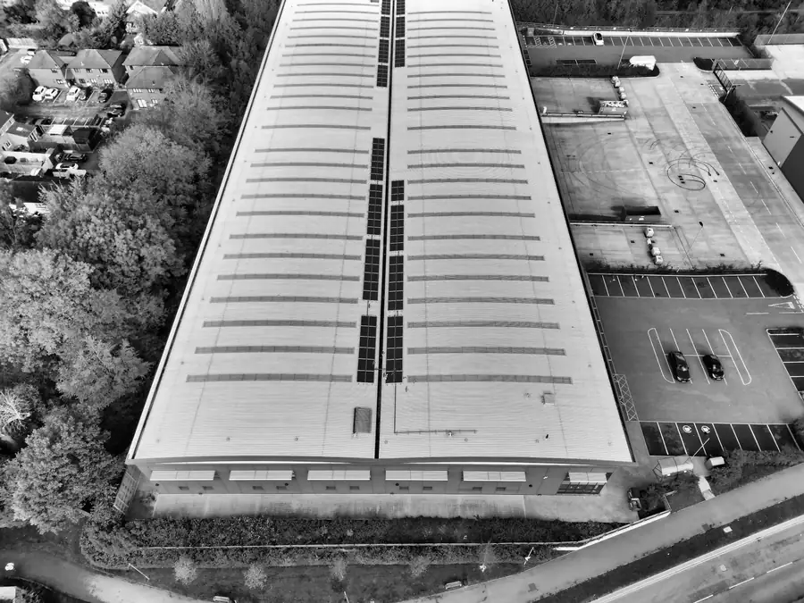 Black and white aerial view of a long warehouse with a strip of solar panels running along the roof ridge