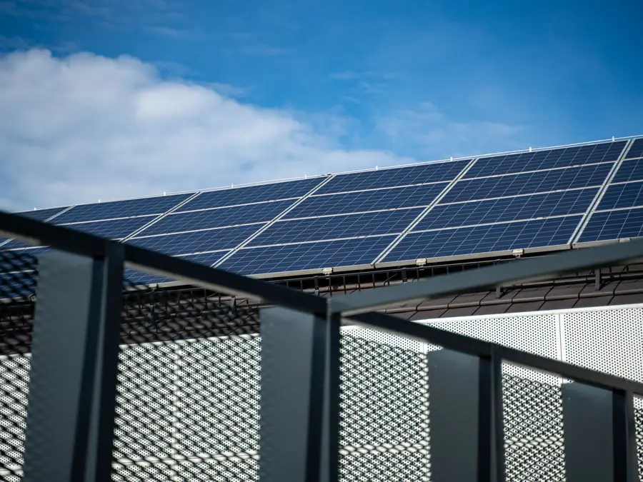 Rooftop solar panels set back behind the metal railing of a modern commercial building