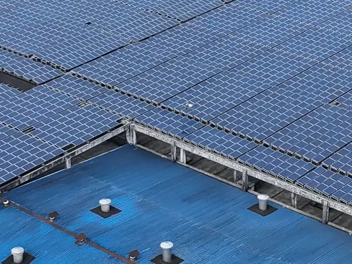Solar panels covering most of a blue-painted factory roof, seen from the roof edge